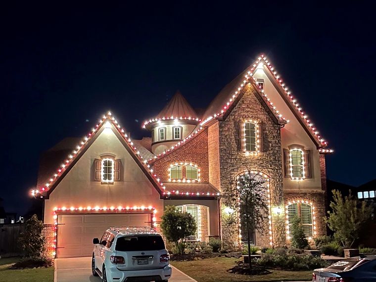 Brick two-story home with warm white roofline lights and lit wreaths