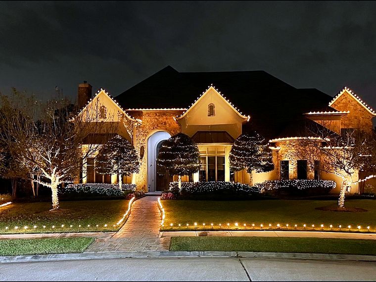 Single-story home with warm roofline lights and lit trees across the yard