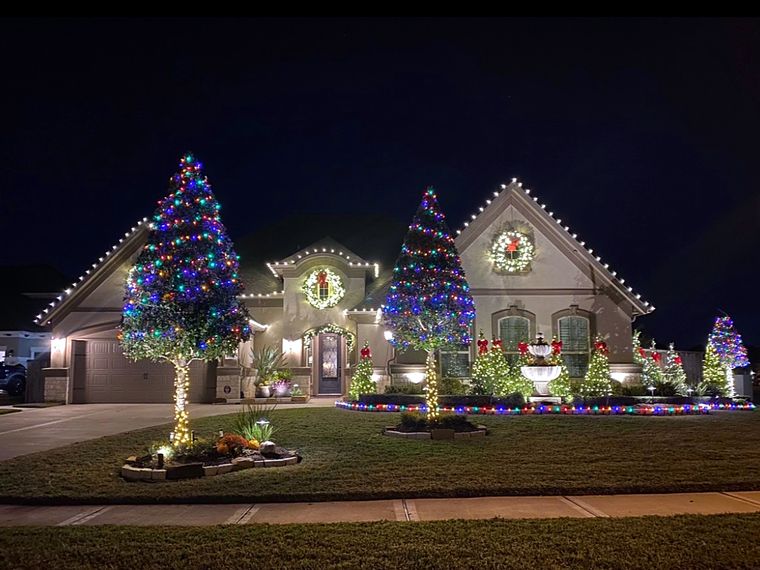 Home with multicolor trees, wreaths and lit landscaping