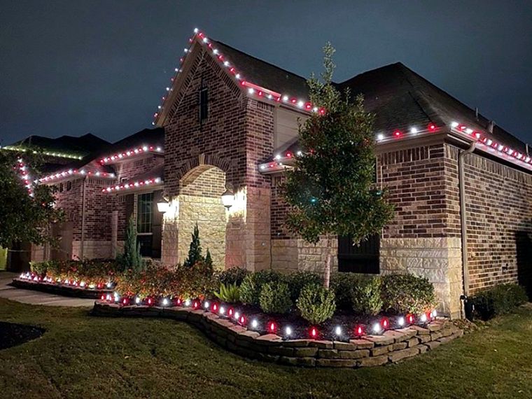 Brick home with red and white roofline lights and lit flower beds